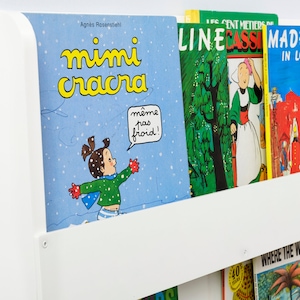 May include: A white bookshelf with a variety of children's books. The books include "Mimi Cracra", "Line Cassi", and "Madeline in London".