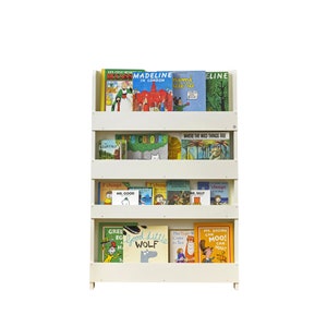 May include: White bookshelf with four shelves filled with colorful children's books. The books include titles like "Madeline", "Where the Wild Things Are", and "Good Little Wolf".