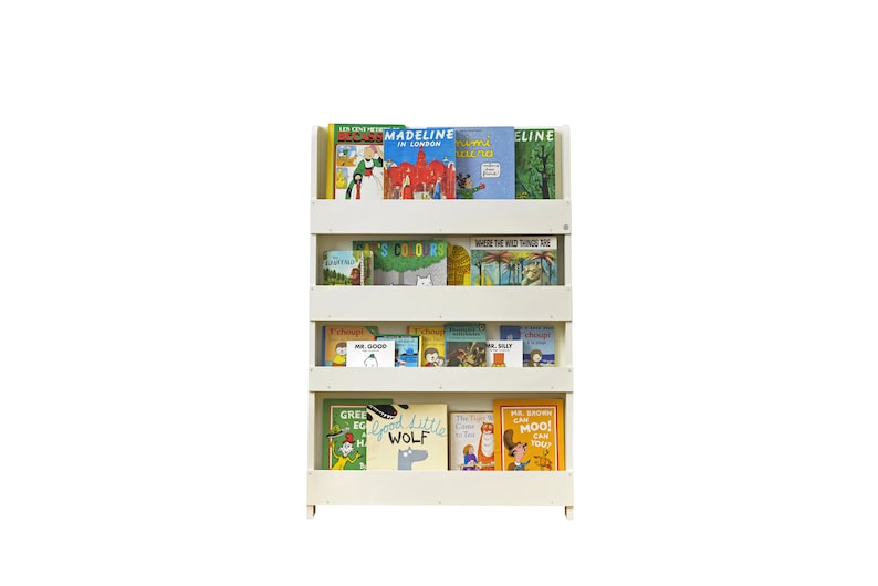 May include: White bookshelf with four shelves filled with colorful children's books. The books include titles like "Madeline", "Where the Wild Things Are", and "Good Little Wolf".