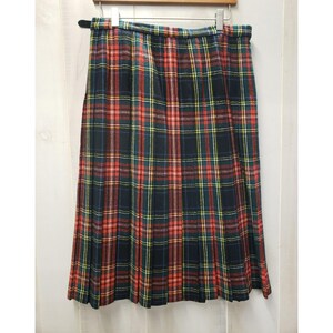Op de afbeelding: Een geplooide geruite rok in rood, groen, geel en marineblauw. De rok hangt aan een houten hanger. De stof lijkt een middelzwaar materiaal te zijn. De rok is ongeveer 76 cm lang.