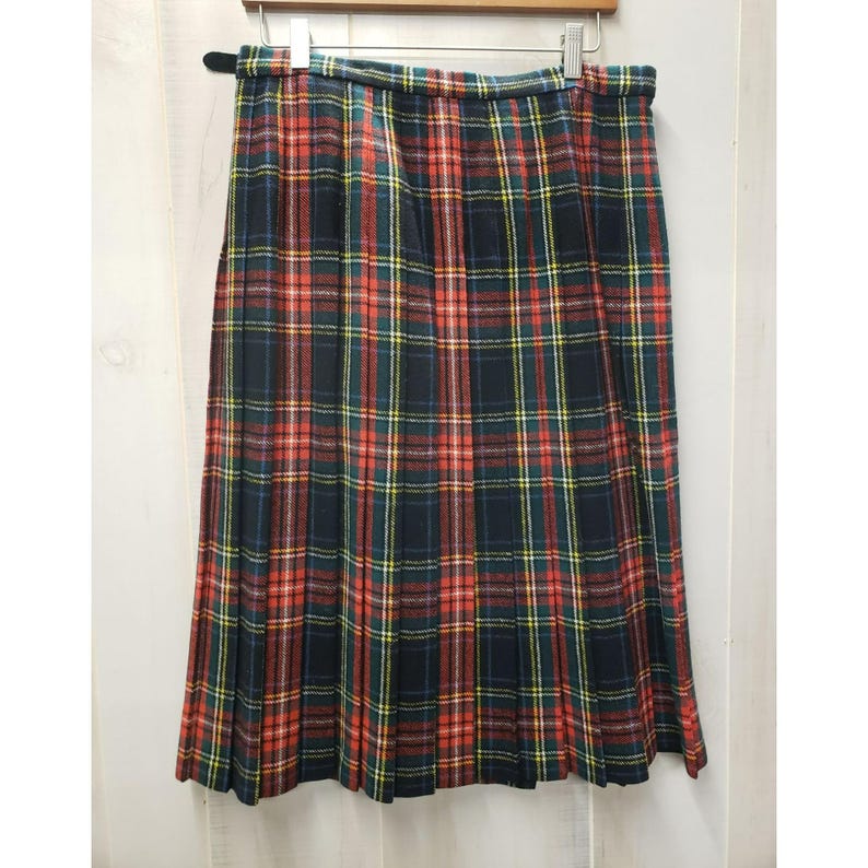 Op de afbeelding: Een geplooide geruite rok in rood, groen, geel en marineblauw. De rok hangt aan een houten hanger. De stof lijkt een middelzwaar materiaal te zijn. De rok is ongeveer 76 cm lang.