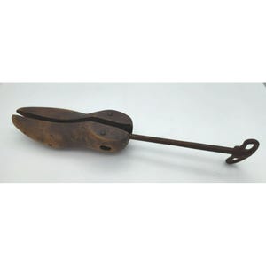 May include: A vintage wooden shoe stretcher with a metal screw and handle. The shoe form is brown with a split toe design. The metal components are a dark, rusty color.