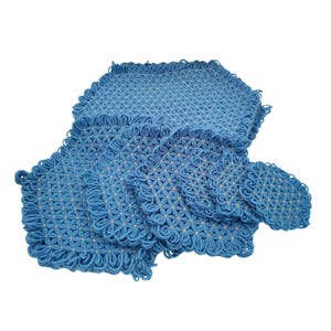 May include: A set of six blue crocheted mats of varying sizes, each featuring a repeating star-like pattern with small beige centers and looped edges. The mats are arranged in a cascading stack, showcasing the intricate yarn work and texture.