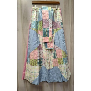 May include: A long skirt featuring a patchwork design with various floral and geometric patterns in shades of light blue, pink, green, and cream. The garment includes a central vertical panel and a solid light blue side section with a pink trim.