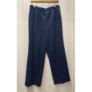 May include: Navy blue wide-leg pants hanging on a wooden hanger. The pants have a smooth, satin-like texture and a high waist. The fabric drapes in soft folds, and the pants appear to be a formal or dressy style. The pants are a solid color.