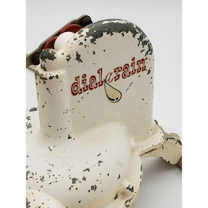 May include: Close-up of a vintage white and black "dial-a-rain" sprinkler system component. The text "dial-a-rain" is in red and the image includes a green water droplet. The paint is chipped, giving it a rustic look.