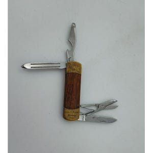 May include: A vintage multi-tool with a wooden handle and several stainless steel attachments, including a bottle opener, scissors, and a small knife. The handle has a brass accent and a small inscription.