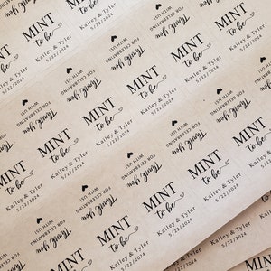 May include: A close-up of several brown paper favour tags with the text "Mint to be" and the names "Kailey & Tyler" and the date "5/22/2024". The tags are decorated with a small heart.