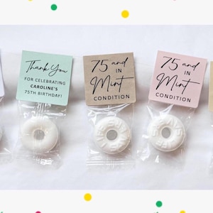 May include: Five small cellophane bags each containing a white mint candy. Each bag has a different colored tag with black text. The tags read "75 and in Mint Condition" and "Thank You for Celebrating Caroline's 75th Birthday!"