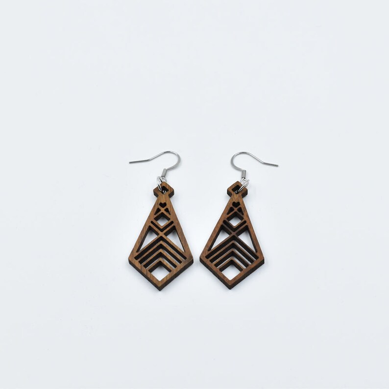 May include: A pair of geometric wooden earrings with a diamond shape. The earrings are a dark brown color and feature a layered design with silver-colored ear wires. The earrings are displayed against a white background.