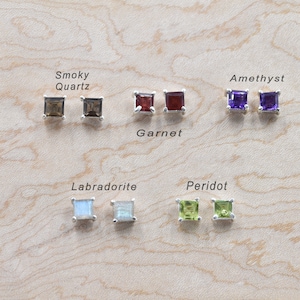 May include: A set of 10 silver stud earrings featuring various coloured gemstones. The gemstones are smoky quartz, garnet, amethyst, labradorite, and peridot.