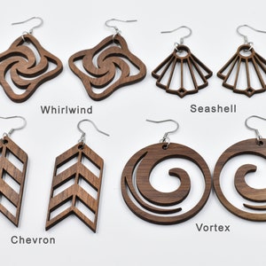 Peut inclure: Une collection de boucles d'oreilles en bois de différentes formes : Tourbillon, Coquillage, Chevron et Vortex. Les boucles d'oreilles sont marron avec des crochets argentés. Les noms des modèles sont imprimés en dessous.