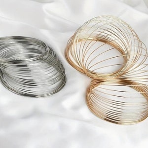 Könnte beinhalten: Zwei Sätze übereinander gestapelter Metallringe, ein Satz ist silberfarben und der andere goldfarben. Die Ringe sind dünn und filigran und in einer Spiralform angeordnet.