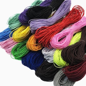 Könnte beinhalten: Eine Sammlung bunter Gummibänder in verschiedenen Farbtönen, darunter Rot, Grün, Blau, Gelb, Rosa, Lila und Schwarz. Die Bänder sind gebündelt und fächerförmig angeordnet.