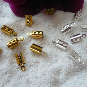 Könnte beinhalten: Nahaufnahme von zwei Sätzen Metall-Endkappen für Schnüre oder Schmuck. Ein Satz ist golden, der andere silbern. Jede Endkappe hat eine kleine Schlaufe oben und drei Löcher an der Seite.