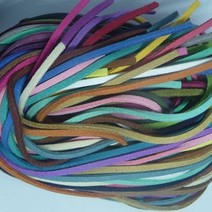 Könnte beinhalten: Ein Bündel bunter Wildlederkordeln in verschiedenen Blautönen, Grüntönen, Brauntönen, Rosatönen, Rottönen und Gelbtönen. Die Kordeln sind in einem lockeren, verhedderten Haufen angeordnet.