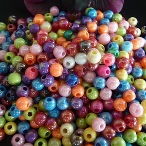 Könnte beinhalten: Ein großer Haufen bunter, irisierender Plastikperlen. Die Perlen sind rund und haben ein Loch in der Mitte. Sie sind perfekt zum Basteln von Schmuck oder anderen Handarbeiten.