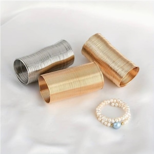 Könnte beinhalten: Drei goldene und silberne Metall-Spiralenarmbänder und ein Perlenarmband mit einem hellblauen Perlenakzent.