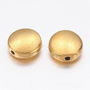 Könnte beinhalten: Zwei goldfarbene Metallperlen mit einem Loch in der Mitte. Die Perlen sind rund und haben eine glatte, matte Oberfläche.