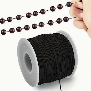 Könnte beinhalten: Eine Spule mit schwarzem elastischem Band zum Schmuckmachen. Das Band ist auf einer weißen Kunststoffspule aufgewickelt.