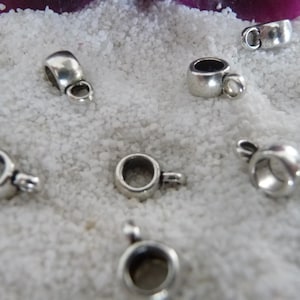 May include: Silver-toned metal bead caps with a round opening and a small loop on the side. The bead caps are arranged on a white surface.
