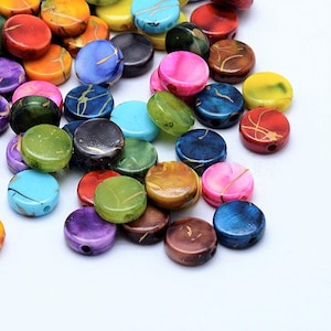 Könnte beinhalten: Sortiment runder, flacher, bunter Perlen mit goldenen Akzenten. Die Perlen sind aus einem glatten, glänzenden Material gefertigt und haben eine Vielzahl von Mustern und Designs.