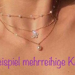 K&ouml;nnte beinhalten: Eine mehrreihige goldene Halskette mit einem Perlenanh&auml;nger und einem Schmetterlingsanh&auml;nger. Die Kette befindet sich am Hals eines Models.