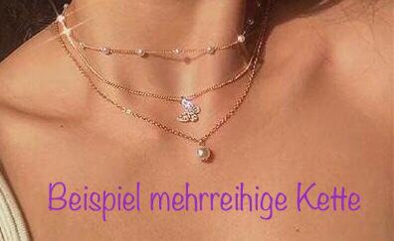 K&ouml;nnte beinhalten: Eine mehrreihige goldene Halskette mit einem Perlenanh&auml;nger und einem Schmetterlingsanh&auml;nger. Die Kette befindet sich am Hals eines Models.