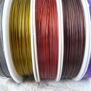 Könnte beinhalten: Fünf Spulen mit metallischem Garn in Silber, Gold, Rot, Braun und Lila. Das Garn ist auf weißen Spulen aufgewickelt.