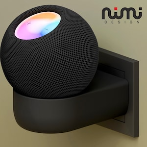 Może przedstawiać: Czarny inteligentny głośnik z kolorowym wyświetlaczem świetlnym na górze, zamontowany do gniazdka ściennego. Głośnik jest oznaczony jako "nimi DESIGN".