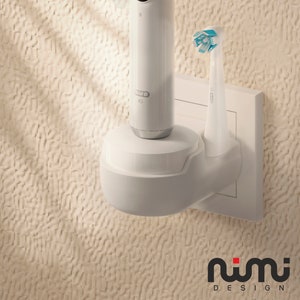 Può includere: Spazzolino elettrico bianco e base di ricarica montati su una presa di corrente bianca. Lo spazzolino da denti ha una testina di spazzola blu. La base è etichettata "Oral-B".