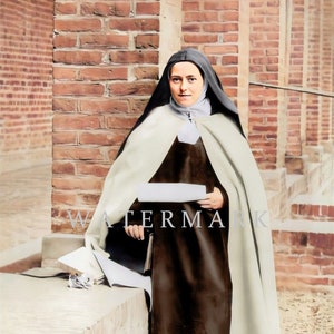 May include: A woman wearing a white and brown habit stands in front of a brick wall. She is holding a white piece of paper in her hands.