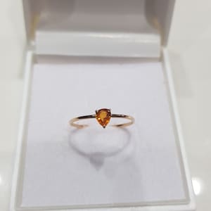 Könnte beinhalten: Ein einfacher goldener Ring mit einem tropfenförmigen orangefarbenen Edelstein.