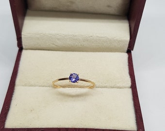 Puede incluir: Un delicado anillo de banda de oro con una pequeña piedra preciosa redonda de color púrpura engastada en el centro.