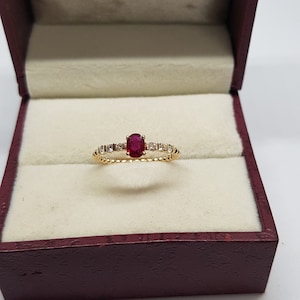 May include: A gold ring with a red oval gemstone surrounded by smaller white gemstones.