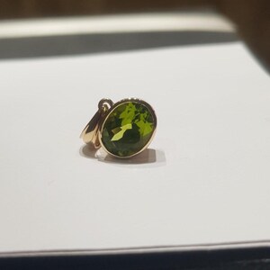 May include: A gold pendant featuring a large, oval-shaped green gemstone.
