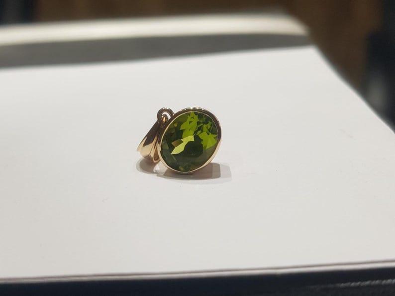 May include: A gold pendant featuring a large, oval-shaped green gemstone.