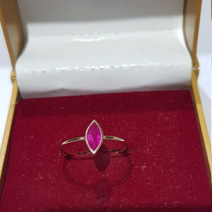 May include: A gold ring with a marquise-shaped ruby gemstone. The ring is in a red velvet box.