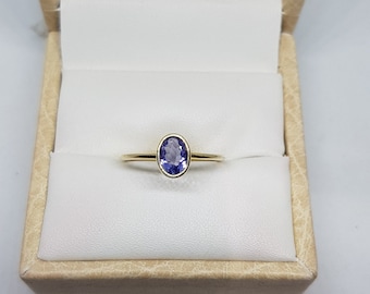 Puede incluir: Un anillo de oro con una piedra ovalada de color púrpura en una caja de anillo.