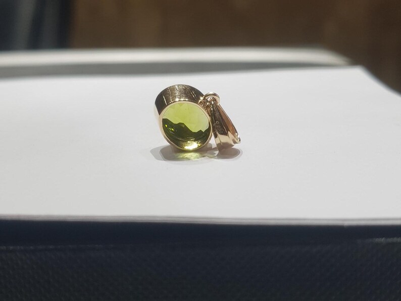 May include: A gold pendant featuring a round green gemstone. The pendant has a simple design and is ideal for adding a touch of elegance to any outfit.