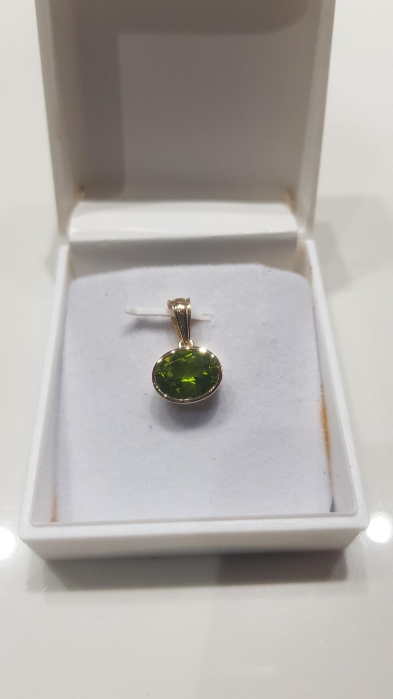 May include: A gold pendant featuring a green oval gemstone.