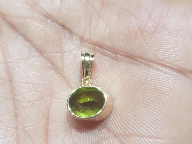 May include: A gold pendant featuring a green gemstone. The pendant is hallmarked 14K.
