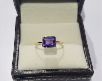 Puede incluir: Un anillo de oro con una amatista rectangular de color púrpura.