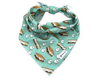 May include: A triangular pet bandana in a light mint green color featuring a repeating pattern of s'mores and white marshmallows. A small white rectangular fabric tag with the text Stella Mae is sewn onto the lower right corner.