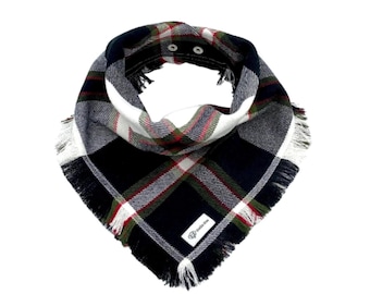 May include: A triangular bandana featuring a dark navy blue, white, and forest green plaid pattern with thin red accent lines. The fabric has a frayed edge finish and two silver-toned metal snap fasteners at the neck. A small white label reads Stella Mae.