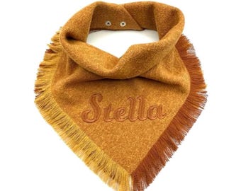 May include: A mustard yellow bandana with a herringbone weave pattern and a fringed edge. The name Stella is embroidered in a cursive font across the center. The garment features two silver-toned metal snap buttons at the neck closure.