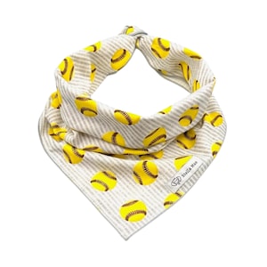 May include: A white and grey striped bandana with a yellow softball pattern. The bandana has a small white tag with the text "Stella & Max" on it.