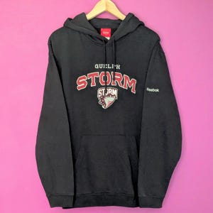 May include: Black hooded sweatshirt with the text "Guelph Storm" and a red and white logo. The Reebok logo is on the right sleeve.