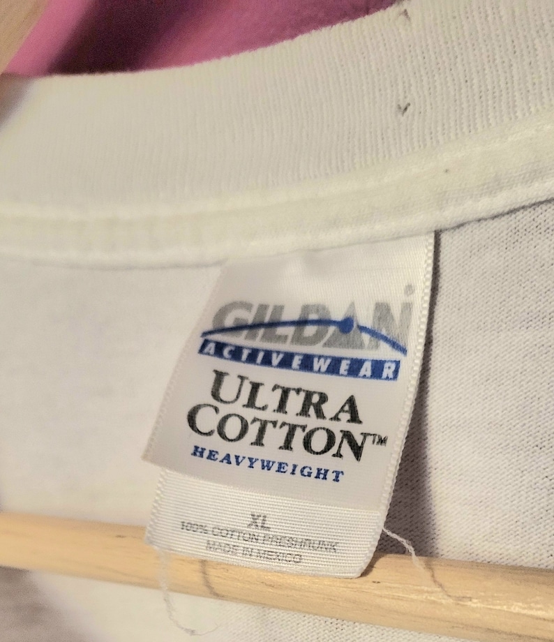 May include: White Gildan Ultra Cotton Heavyweight t-shirt tag with blue text. The tag says "Gildan Activewear Ultra Cotton Heavyweight" and "100% Cotton Preshrunk Made in Mexico". The size tag says "XL".