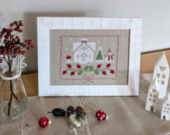 May include: White framed cross-stitch embroidery depicting a white house with red berries and a snowman in a snowy winter scene.